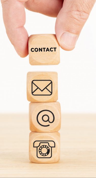 Contact us concept. Hand holding a wooden block with text and a pile of dices with communication icon. Copy space